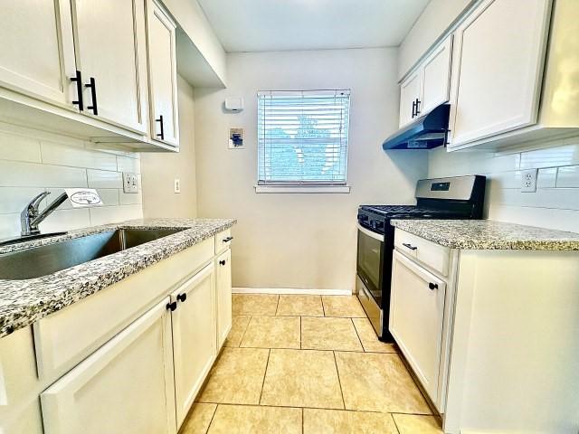 kitchen with light tile patterned floors, stainless steel gas range oven, tasteful backsplash, under cabinet range hood, and a sink