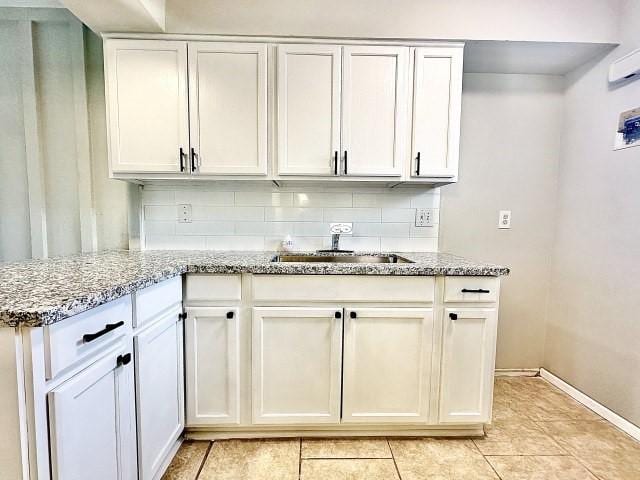 kitchen featuring white cabinetry, a sink, decorative backsplash, and light stone countertops