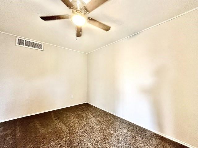 empty room featuring dark carpet, visible vents, and a ceiling fan