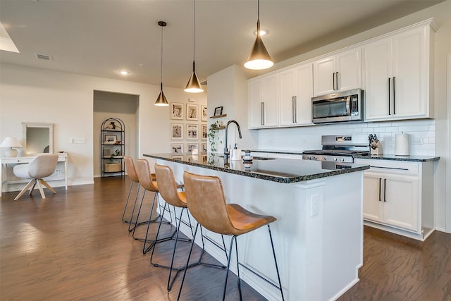 kitchen featuring a center island with sink, visible vents, decorative backsplash, appliances with stainless steel finishes, and dark wood-type flooring