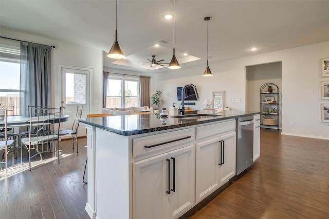 kitchen featuring dark wood finished floors, dishwasher, dark stone countertops, a kitchen island with sink, and a sink