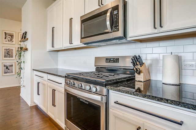 kitchen featuring white cabinets, appliances with stainless steel finishes, dark stone countertops, wood finished floors, and backsplash