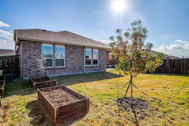 back of property featuring a garden, a lawn, a fenced backyard, roof with shingles, and brick siding