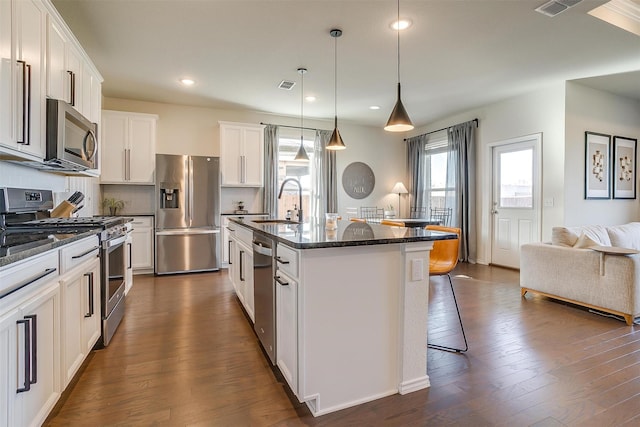 kitchen with dark wood-style flooring, a sink, a kitchen breakfast bar, appliances with stainless steel finishes, and a center island with sink