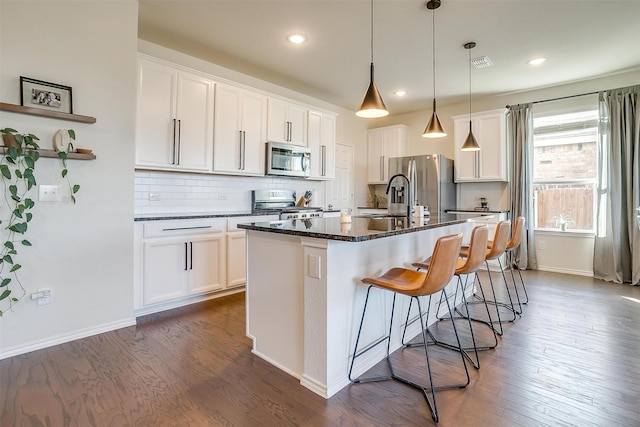 kitchen with a center island with sink, visible vents, dark wood-type flooring, stainless steel appliances, and backsplash