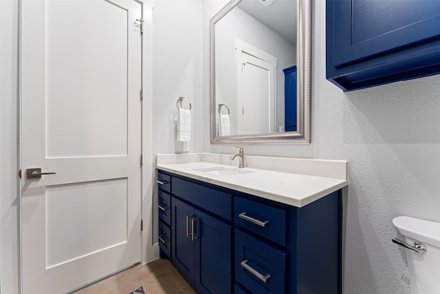 half bathroom featuring toilet, a textured wall, and vanity