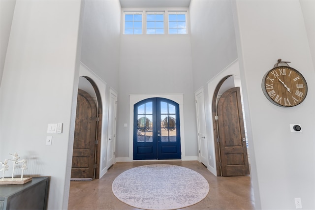 foyer with arched walkways, french doors, concrete floors, and a towering ceiling