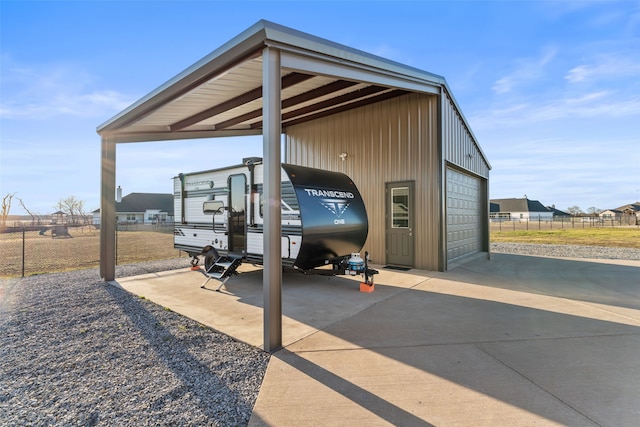 view of vehicle parking with driveway, a carport, a detached garage, and fence