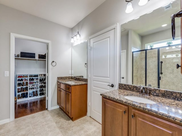 full bath with two vanities, a sink, baseboards, a spacious closet, and a shower stall