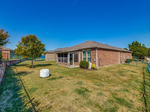 rear view of house featuring a sunroom, a fenced backyard, a lawn, and brick siding