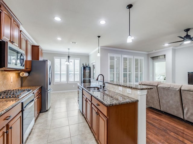 kitchen with a sink, ornamental molding, appliances with stainless steel finishes, tasteful backsplash, and dark stone countertops