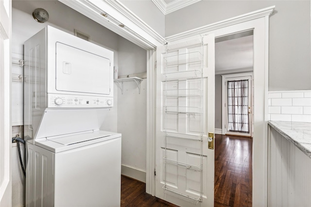 clothes washing area with dark wood-style floors, crown molding, stacked washer and dryer, laundry area, and baseboards