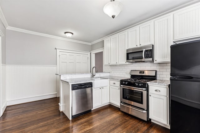 kitchen featuring a peninsula, a sink, appliances with stainless steel finishes, wainscoting, and dark wood-style floors