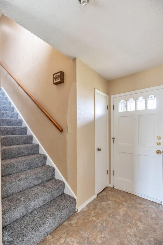 foyer entrance with stairway and baseboards