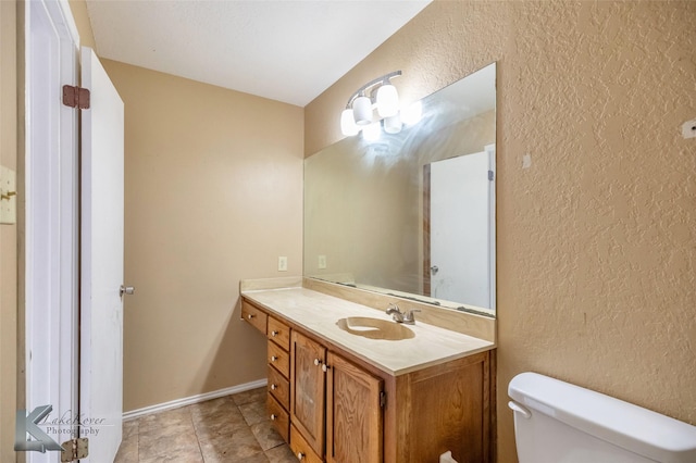 bathroom featuring baseboards, a textured wall, vanity, and toilet