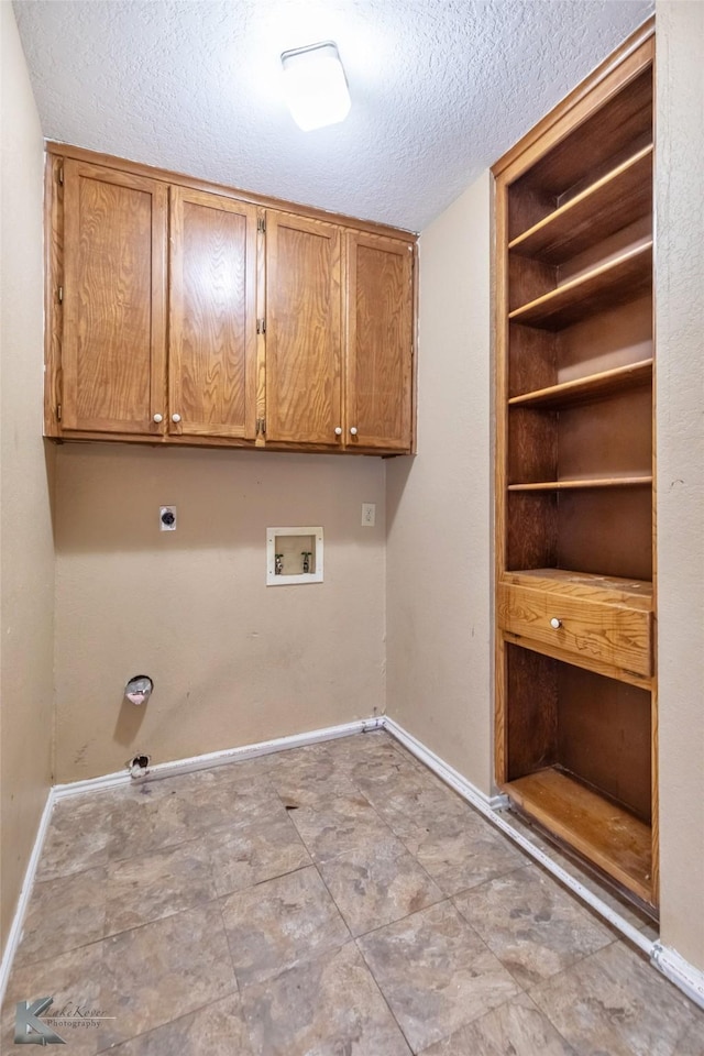 laundry room with a textured ceiling, washer hookup, cabinet space, and baseboards