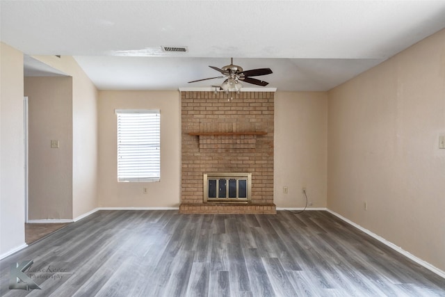 unfurnished living room featuring a brick fireplace, baseboards, visible vents, and wood finished floors