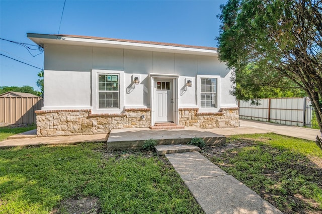 bungalow-style house featuring stone siding, a front yard, fence, and stucco siding