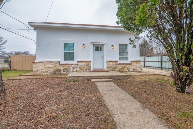 view of front of property featuring stone siding, fence, and stucco siding