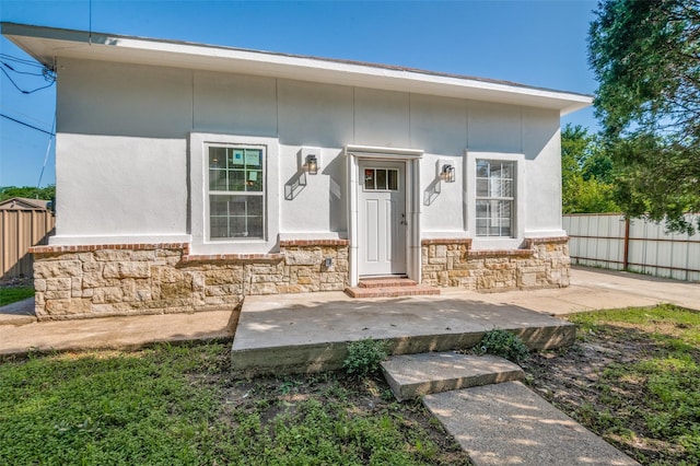 view of front of house with stone siding, fence, and stucco siding