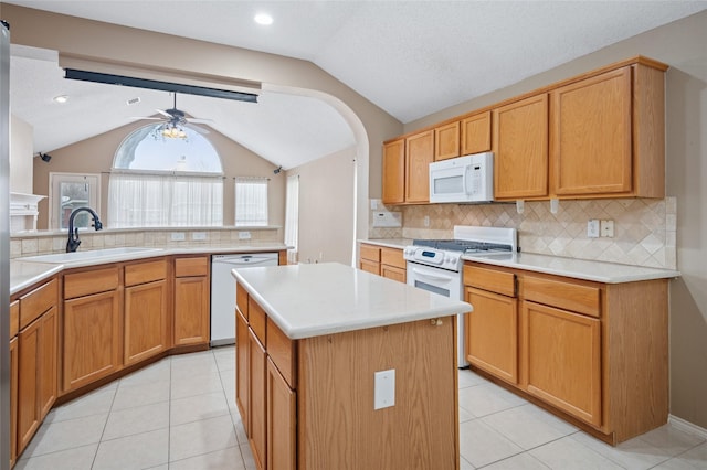 kitchen with white appliances, lofted ceiling, a kitchen island, light countertops, and a sink