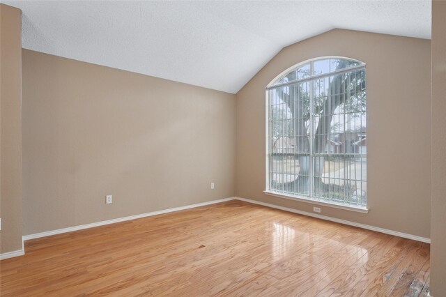 unfurnished room with baseboards, vaulted ceiling, a textured ceiling, and light wood finished floors