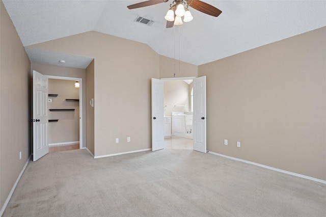 unfurnished bedroom with washer / dryer, visible vents, vaulted ceiling, and light colored carpet