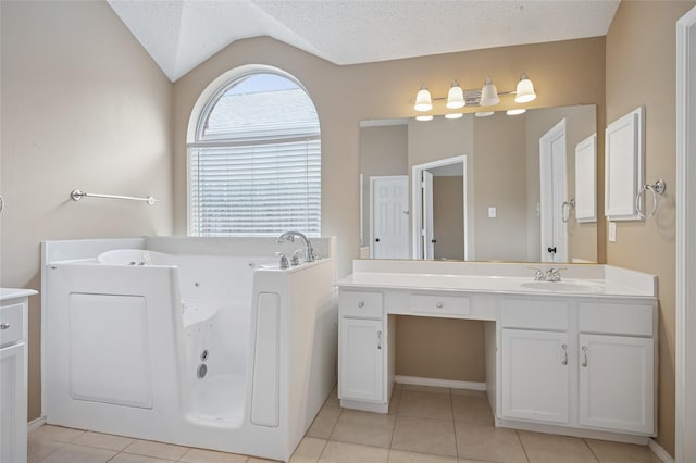 bathroom featuring vaulted ceiling, a textured ceiling, vanity, a tub with jets, and tile patterned floors