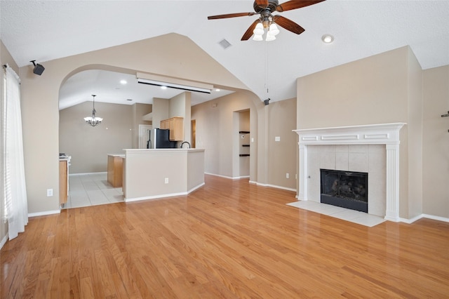 unfurnished living room with arched walkways, vaulted ceiling, a fireplace, and ceiling fan with notable chandelier