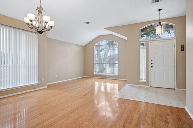 entryway with lofted ceiling, visible vents, baseboards, light wood finished floors, and an inviting chandelier