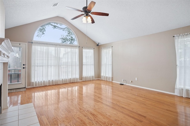 unfurnished living room featuring a fireplace, light wood finished floors, vaulted ceiling, a textured ceiling, and ceiling fan