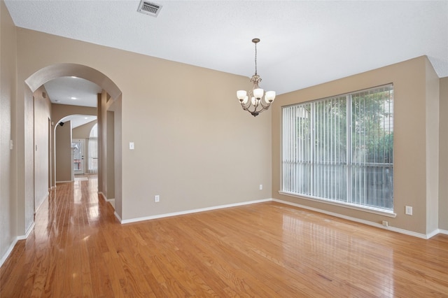 unfurnished room with light wood-type flooring, baseboards, visible vents, and arched walkways