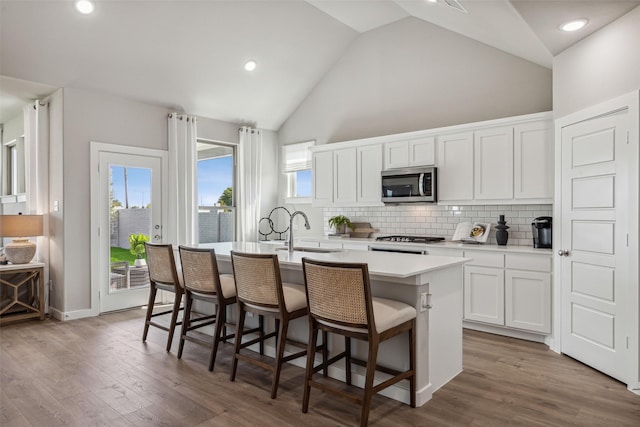 kitchen with a breakfast bar area, stainless steel microwave, a sink, and an island with sink