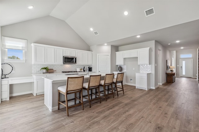 kitchen with stainless steel microwave, a center island with sink, visible vents, and white cabinetry