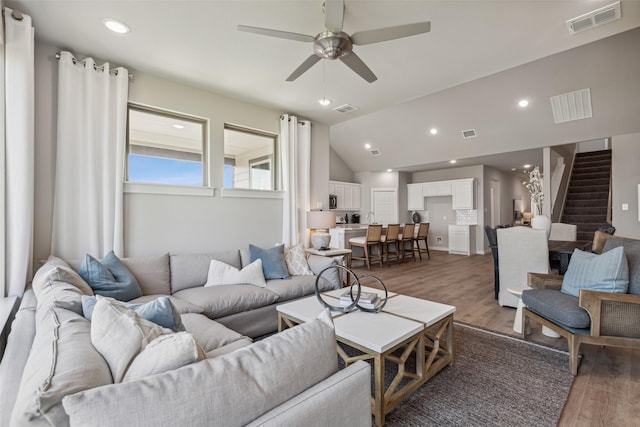 living room featuring visible vents, vaulted ceiling, light wood-style flooring, and stairs