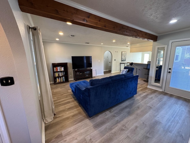 living area featuring arched walkways, ornamental molding, a textured ceiling, and wood finished floors