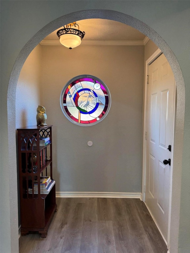 interior space featuring baseboards, arched walkways, wood finished floors, and ornamental molding