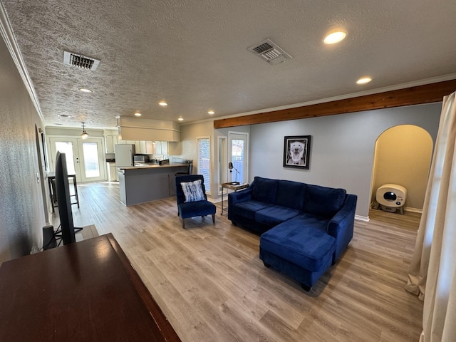 living room with ornamental molding, visible vents, light wood-style flooring, and a textured ceiling