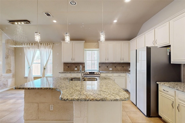 kitchen featuring a kitchen island with sink, a sink, visible vents, freestanding refrigerator, and decorative backsplash