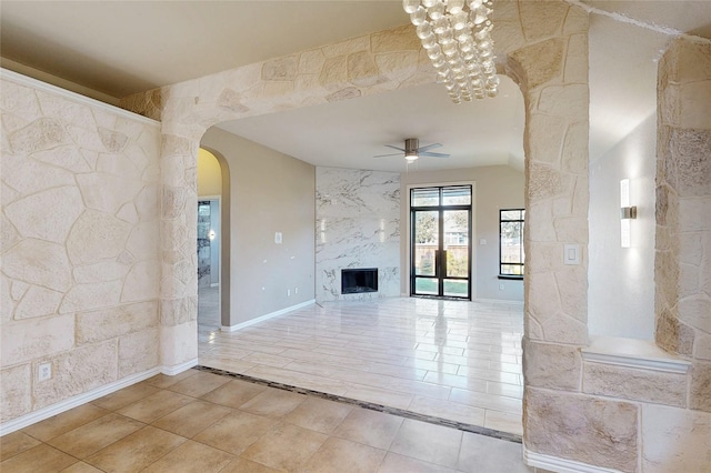 unfurnished living room featuring baseboards, arched walkways, a ceiling fan, tile patterned flooring, and a fireplace