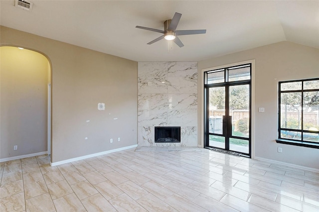 unfurnished living room with arched walkways, lofted ceiling, a fireplace, visible vents, and a ceiling fan