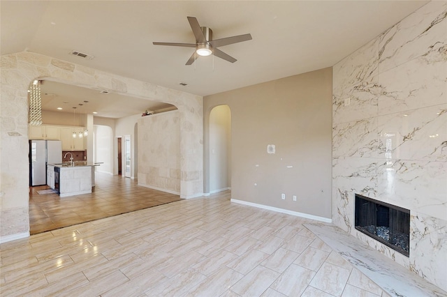 unfurnished living room with arched walkways, a ceiling fan, a high end fireplace, a sink, and baseboards