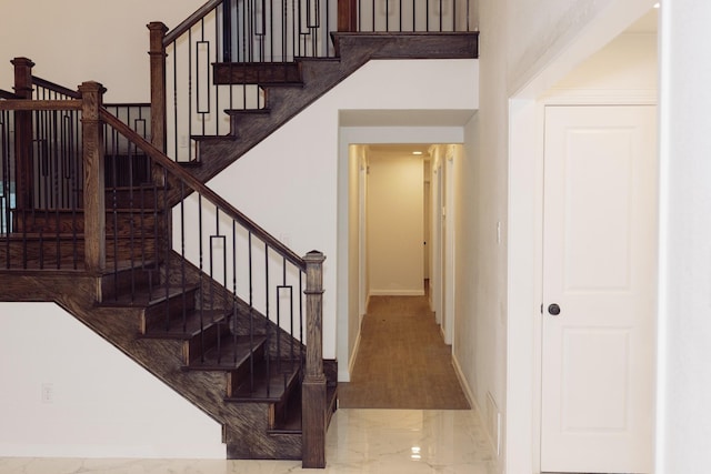 stairway with marble finish floor, a towering ceiling, and baseboards