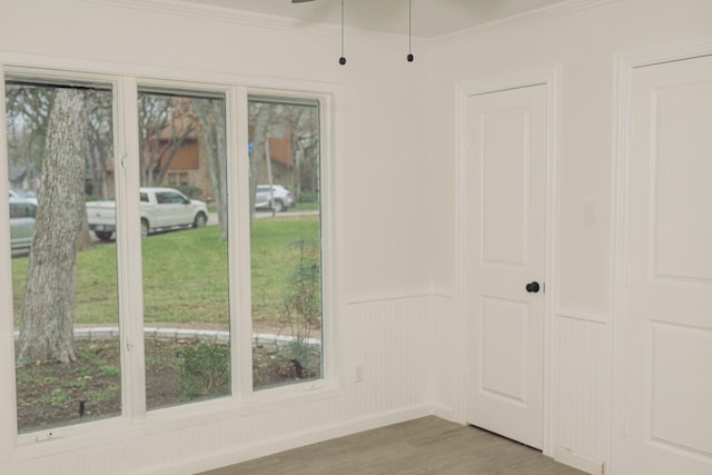 interior space featuring a wainscoted wall, ceiling fan, crown molding, and wood finished floors