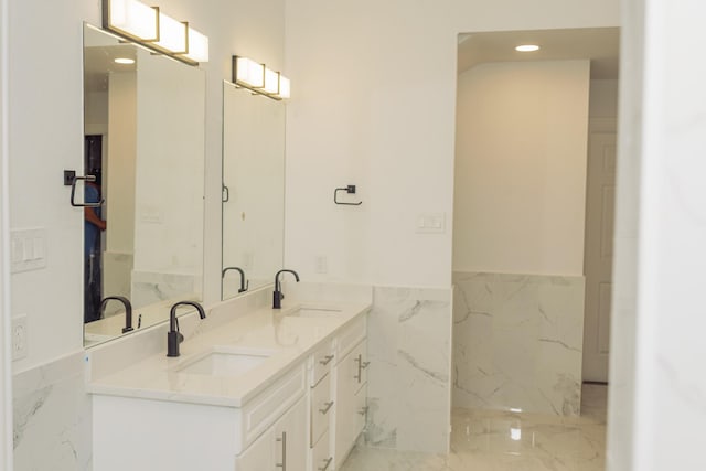 bathroom with marble finish floor, double vanity, wainscoting, and a sink