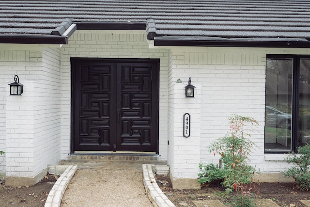 view of exterior entry featuring a tiled roof and brick siding