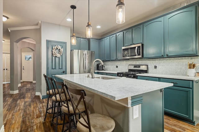 kitchen featuring arched walkways, dark wood-style flooring, a sink, appliances with stainless steel finishes, and decorative backsplash