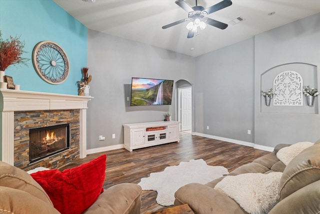 living room with baseboards, visible vents, arched walkways, wood finished floors, and a stone fireplace