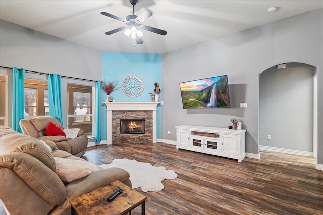 living room featuring arched walkways, a fireplace, wood finished floors, a ceiling fan, and baseboards