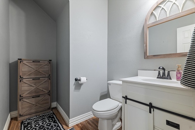 half bathroom featuring vanity, wood finished floors, toilet, and baseboards